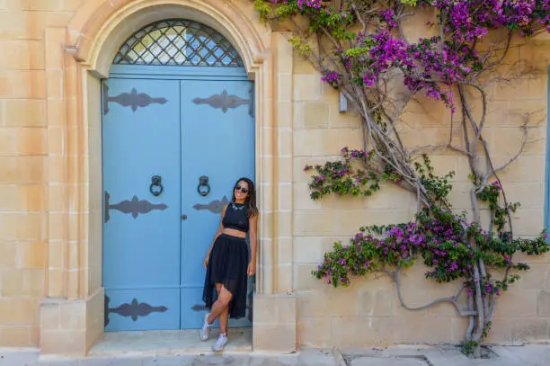 Beautiful young woman next to blue door and wall-growing tree