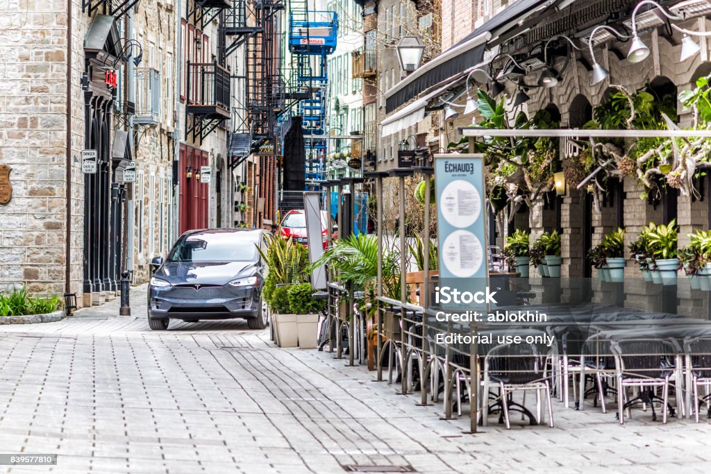Tesla modelo X conducir en camino de adoquines en ciudad vieja baja calle llamada rue Sault-au-Matelot por restaurantes, tiendas y tiendas de souvenirs de azul - Foto de stock de Quebec libre de derechos