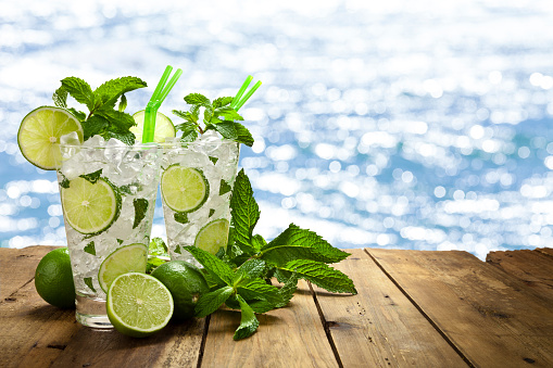 Two mojito cubano drinks against defocused shiny sea water. Copy space available for text and/or logo on background. Predominant colors are blue, green and brown. Composite photo taken with Canon EOS 5D Mk II and Canon EF lenses