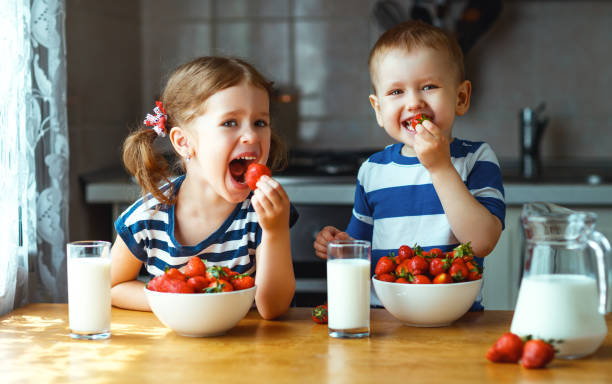 幸せな子供の兄と妹のミルクとイチゴを食べて - healthy lifestyle people eating sister ストックフォトと画像