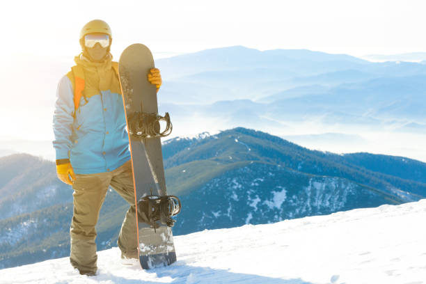 istock Young snowboarder standing next to snowboard thrusted into snow with beautiful scenery on background 839842518