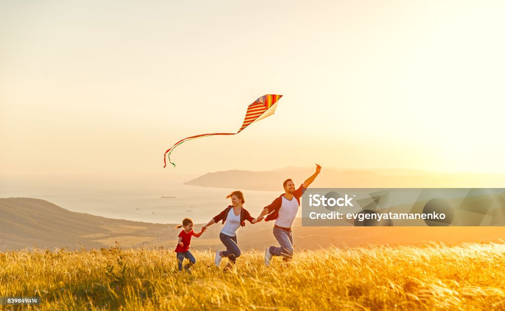 Felice padre di famiglia di madre e figlia bambino lancia un aquilone sulla natura al tramonto - Foto stock royalty-free di Famiglia