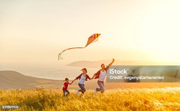 Felice Padre Di Famiglia Di Madre E Figlia Bambino Lancia Un Aquilone Sulla Natura Al Tramonto - Fotografie stock e altre immagini di Famiglia