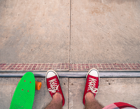 Low section of a male skater in red sneakers with a green penny board on the half-pipe.