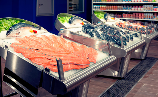 Salmon fillets and whole fish on cooled market display, toned image