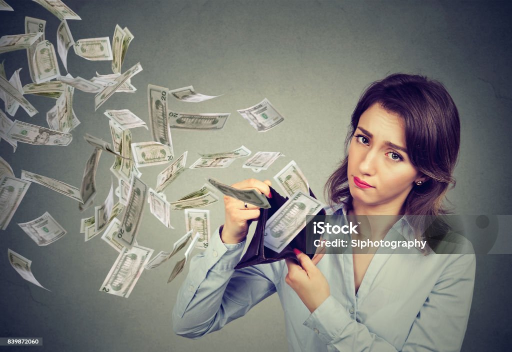 Sad woman showing her wallet with money dollar banknotes flying out away Wasting Money Stock Photo