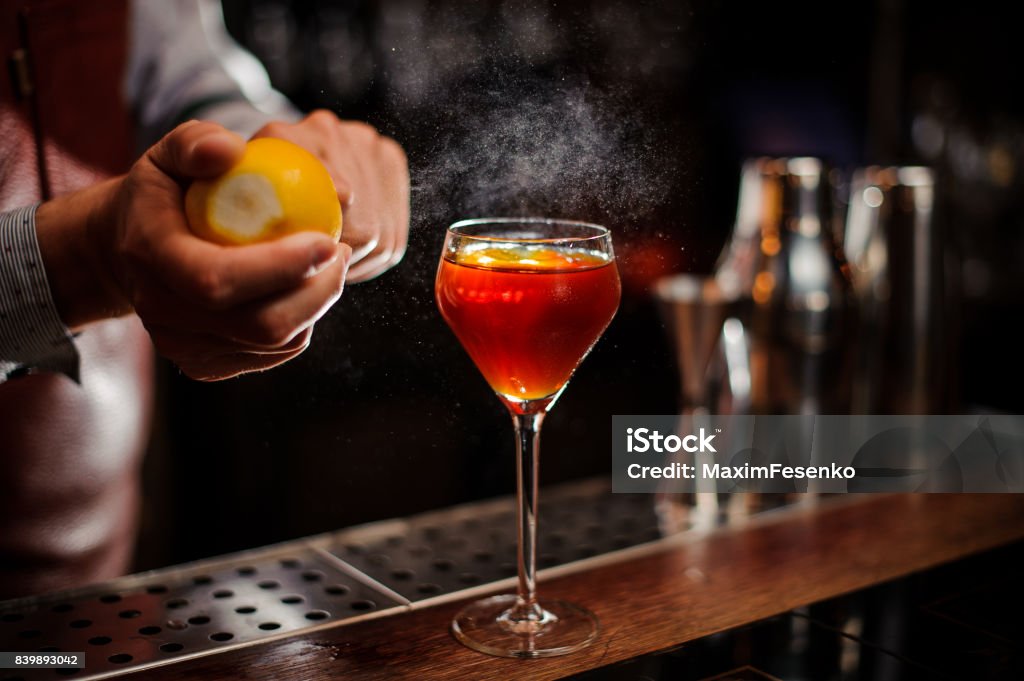 Bartender is adding lemon zest to the cocktail at bar counter Bartender is adding lemon zest to the red cocktail at bar counter Cocktail Stock Photo