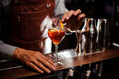 Bartender with glass and lemon peel preparing cocktail at bar