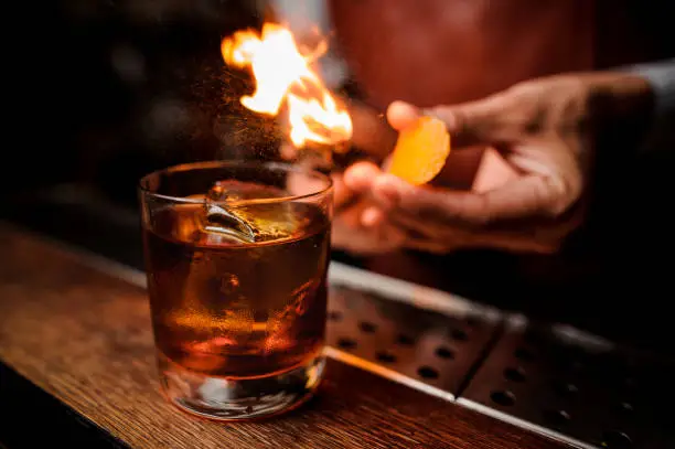 Photo of The bartender makes flame above cocktail close up
