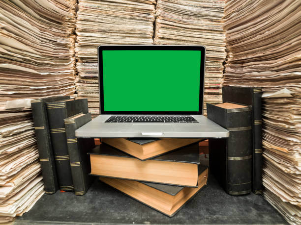 laptop on desk in printed media library - book stack embracing business imagens e fotografias de stock