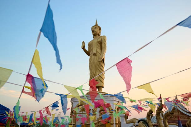 Standing golden Buddha statue in Oudomxay Standing big golden Buddha statue in the temple on the hill in Oudomxay on the background of twilight sky theravada photos stock pictures, royalty-free photos & images