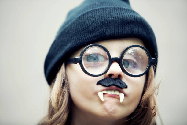 funny portrait of young boy with hat wearing big glasses, fake vampire teeth and a mustache