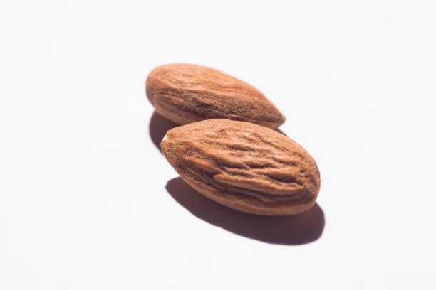 Close up of two almonds against white with strong shadow.