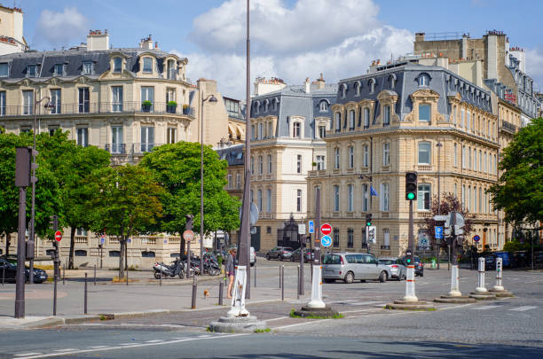 Paris,  France - June 4, 2017: Old Parisian four-story buildings with attic roofs are located at corner Cours Albert 1er and Rue Francois 1er. There are some cars moving on the road. The same time parked bikes and autos are visible along of it. Unidentified woman walks small dog nearby crosswalk in the middle. Summer sunny day.