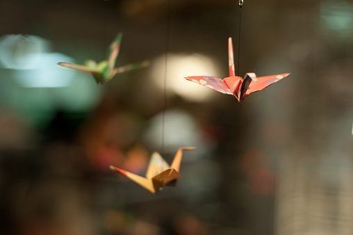 Colored paper folded into three oragami paper cranes hung from string as if flying.