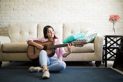 Young woman spending the afternoon sitting on the floor of the living room playing the guitar