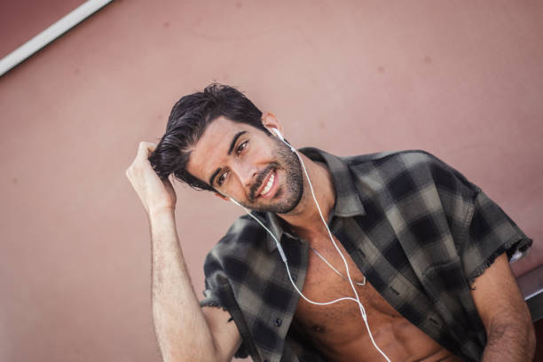 sonriente hombre con auriculares sentado al aire libre - fully unbuttoned audio fotografías e imágenes de stock