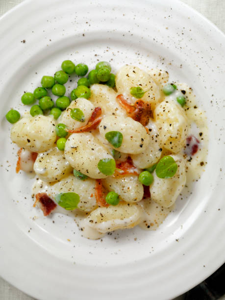 gnocchi in einer cremigen knoblauchsauce mit erbsen und speck - kartoffelknödel essen stock-fotos und bilder