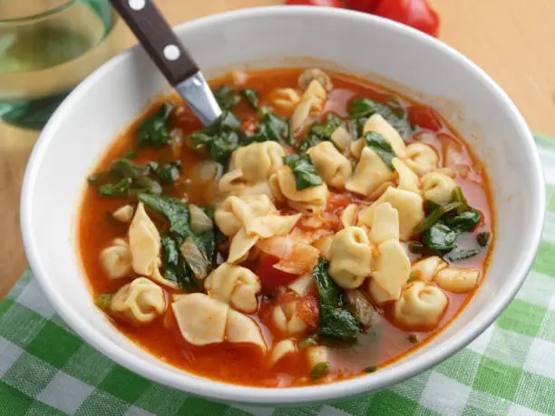 Tomato tortellini spinach soup on a rustic table