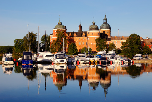 Mariefred, Sweden - August 15, 2017: The morning sun shines at Gripsholm Castle that reflects in the water next to the marina by pleasure boats.