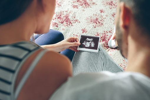 Couple looking at ultrasound of their baby sitting on the bed. Selective background focus on ultrasound