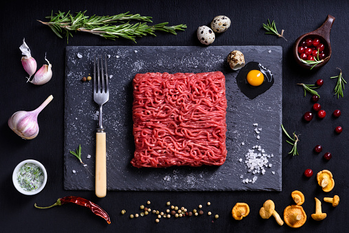 Raw fresh lamb meat with condiments, cooking ingredients on black background. Top view, flat lay.