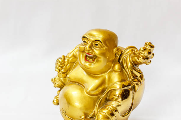Cheerful statue of Laughing Buddha holding an offering bowl, symbolizing prosperity and happiness, set against a stone wall background.