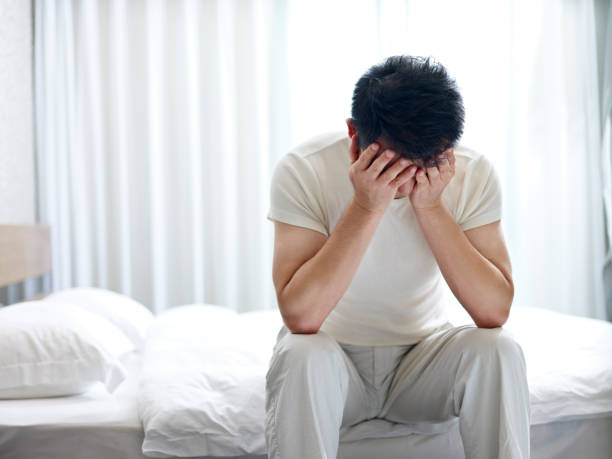 asian man in despair asian man suffering from insomnia sitting on bed head down covering face with hands. facepalm stock pictures, royalty-free photos & images