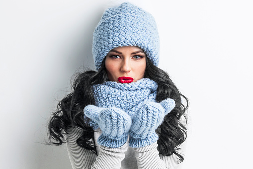 Beautiful woman in blue winter hat, scarf and mittens blowing on palms