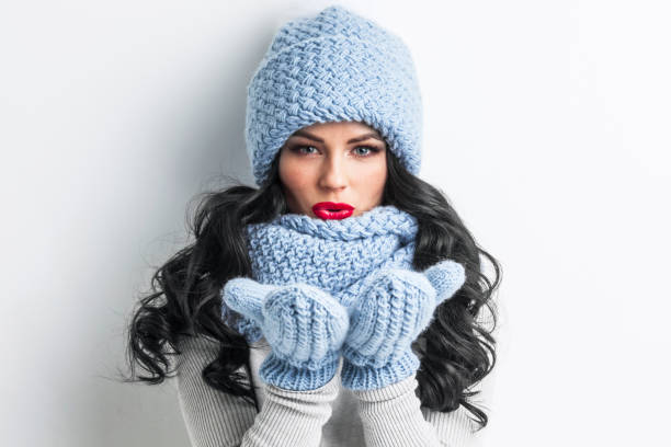 Woman in winter clothes blowing on palms Beautiful woman in blue winter hat, scarf and mittens blowing on palms blowing a kiss stock pictures, royalty-free photos & images