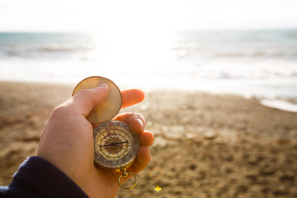 foto de punto de vista del hombre sostiene la brújula con la mano en el fondo del mar y playa - compass exploration the way forward beach fotografías e imágenes de stock