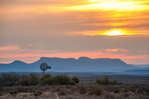 A windmill in the Karoo with a mountain range behind at a spectacular orange cloudy sunset Karoo National Park Beaufort West Western Cape South Africa