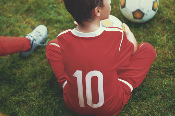 маленький футболист вперед мальчик сидит на траве - soccer child little boys playing стоковые фото и изображения