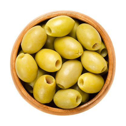 Pitted and marinated green olives in wooden bowl. Fruits of the European olive, Olea europaea. Unripe table olives with yellow to green color. Isolated macro food photo close up from above over white.