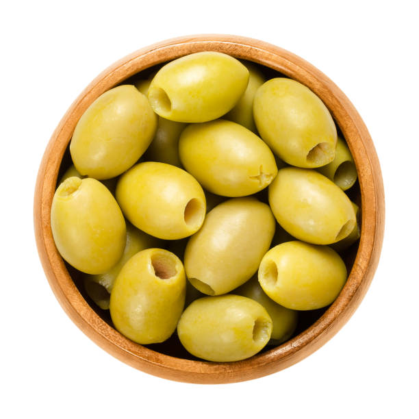 Pitted and marinated green olives in wooden bowl Pitted and marinated green olives in wooden bowl. Fruits of the European olive, Olea europaea. Unripe table olives with yellow to green color. Isolated macro food photo close up from above over white. olive tree cut out stock pictures, royalty-free photos & images