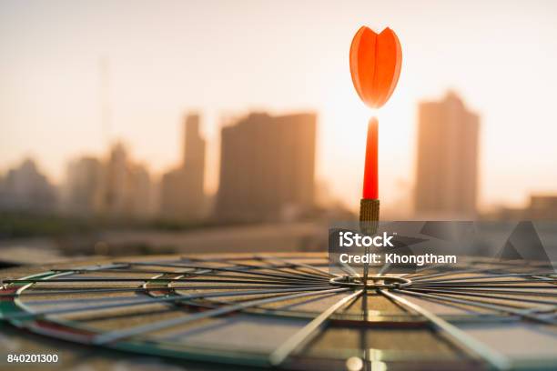 Red Dart Arrow Hitting In The Target Center Of Dartboard With Modern City And Sunset Background Target Business Achieve And Victory Concept Stock Photo - Download Image Now