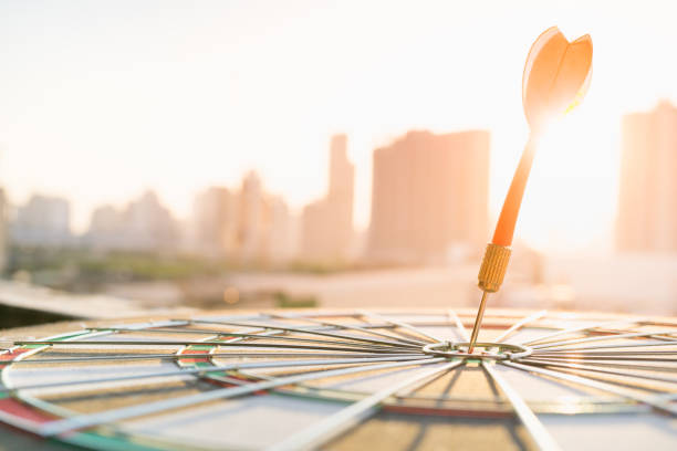 red dart arrow hitting in the target center of dartboard with modern city and sunset background. target business, achieve and victory concept . - sharp curve imagens e fotografias de stock