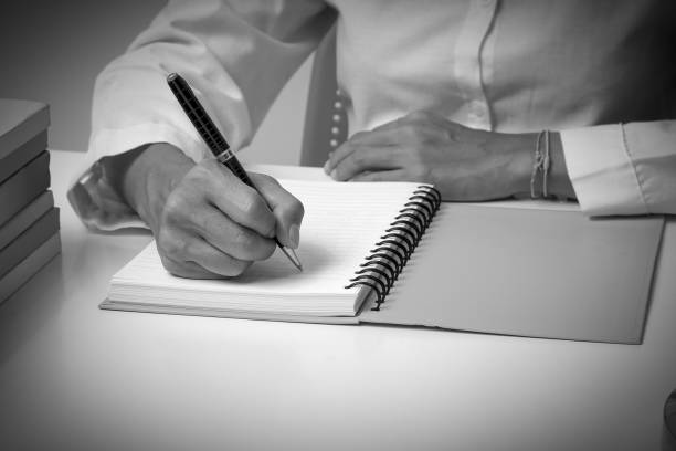 istock Woman writing in spiral notepad placed on bright desktop with the book on the table, As Business or Education Background Concept, Black and white tone. 840206288