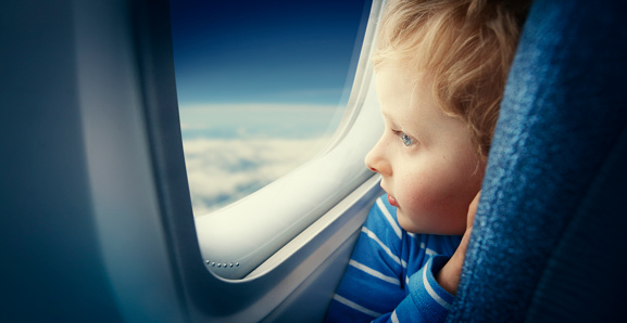 Curious young blonde boy watching sky from airplane window during flight
