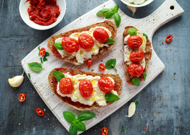 bruschetta di ricotta di pomodoro con pasta di pomodori secchi, pane marrone olio d'oliva e basilico in una tavola di legno bianco. - crostini bruschetta antipasto appetizer foto e immagini stock