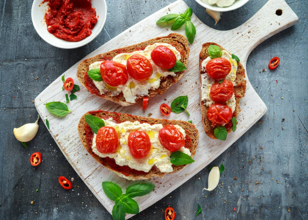 Tomato Ricotta Bruschetta with sun dried tomatoes paste, olive oil brown bread and basil in a white wooden board. Tomato Ricotta Bruschetta with sun dried tomatoes paste, olive oil brown bread and basil in a white wooden board ricotta photos stock pictures, royalty-free photos & images