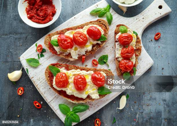 Tomato Ricotta Bruschetta With Sun Dried Tomatoes Paste Olive Oil Brown Bread And Basil In A White Wooden Board Stock Photo - Download Image Now