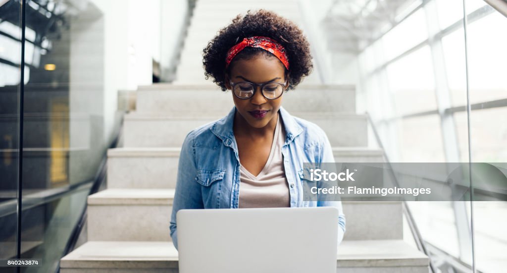 Giovane studente africano concentrato seduto sulle scale usando un laptop - Foto stock royalty-free di Donne