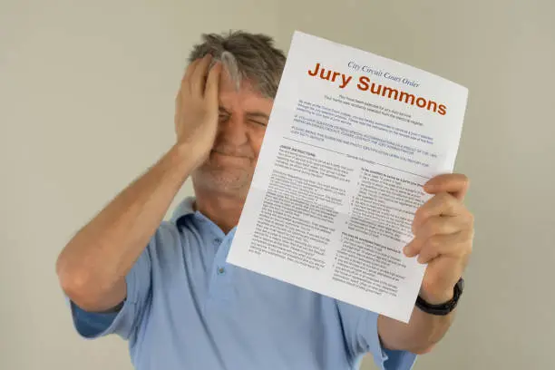 Angry upset man holing out his hand to show the jury duty summons he received in the mail which means he must be a juror on a court case.