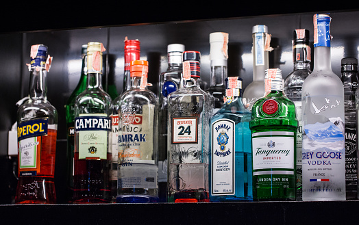 HAMBURG, GERMANY, DECEMBER 2016: Assorted spirit drink bottles behind the bar under low light. Vodka, gin, tequila, Pernod and other drinks are visible.