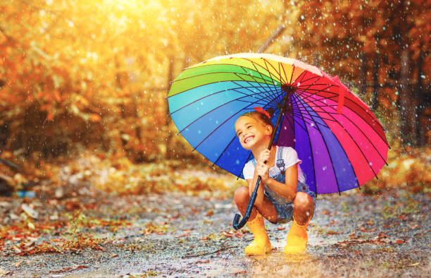 chica de niño divertido feliz con paraguas saltando sobre los charcos en botas de goma - colors color image rainbow umbrella fotografías e imágenes de stock