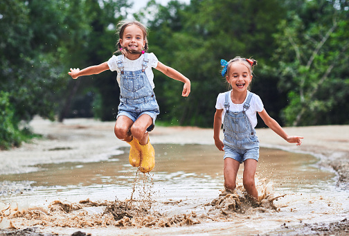 Happy funny sisters twins  child by girl jumping on puddles in rubber boots and laughing