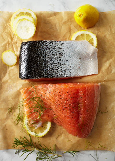 Prepared raw salmon fillets on parchment paper Two raw salmon fillets with silver skin laying on parchment paper with lemon slices and fresh dill. sockeye salmon filet stock pictures, royalty-free photos & images