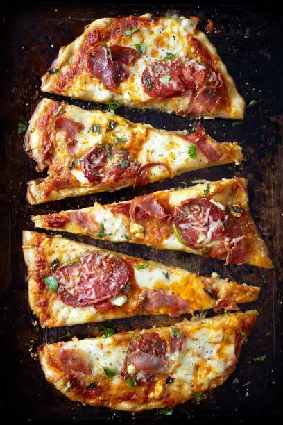 A rustic oval shaped homemade pizza with cheese, sliced heirloom tomatoes, prosciutto and fresh torn basil.