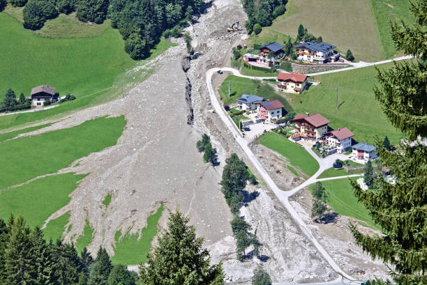 Aerial view of mountain stream in the Austrian Alps blocked after a massive mudflow with excavator and truck working to clean up and small village nearby stock photo